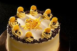 Round yellow birthday cake. Decorative cream decorations on the cake. Black background. photo