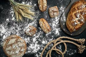 Different bread with flour and spikelets of wheaton black background photo