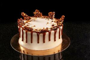 Round white cake with caramel and chocolate puffed rice on a round tray on black background photo