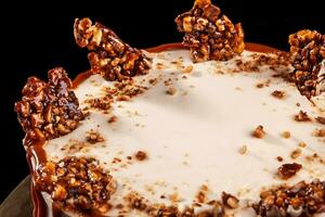 Round white cake with caramel and chocolate puffed rice on a round tray on black background photo