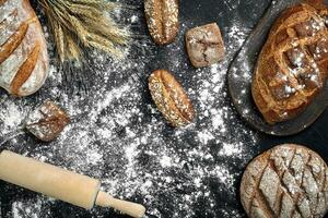 Different bread with flour and spikelets of wheaton black background photo