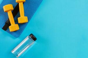 pesas y botella de agua en azul antecedentes. parte superior vista. aptitud física, deporte y sano estilo de vida concepto. foto