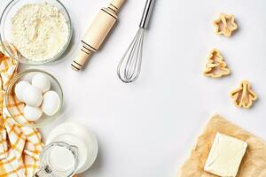 Objects and ingredients for baking, plastic molds for cookies on a white background. Flour, eggs, rolling pin, whisk, milk, butter, cream. Top view, space for text photo