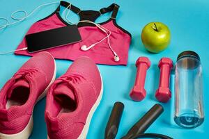 Athlete's set with female clothing, dumbbells and bottle of water on bright blue background photo