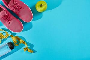Sneakers with measuring tape on cyan blue background. Centimeter in yellow color near pink trainers, close up. photo