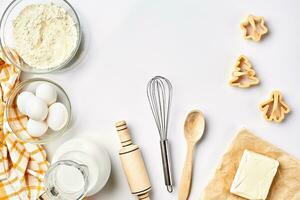 Objects and ingredients for baking, plastic molds for cookies on a white background. Flour, eggs, rolling pin, whisk, milk, butter, cream. Top view, space for text photo