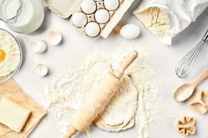 Raw dough ready for kneading on white table. Bakery ingredients, eggs, flour, butter. Shapes for making cookies. photo