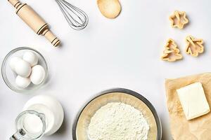 Objects and ingredients for baking, plastic molds for cookies on a white background. Flour, eggs, rolling pin, whisk, milk, butter, cream. Top view, space for text photo