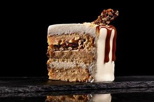 Piece of white cake with caramel and chocolate puffed rice on a black tray on black background photo