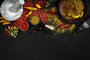 Cooking using fresh ground spices with mortar and small bowls of spice on a black table with powder spillage on its surface, overhead view with copyspace photo