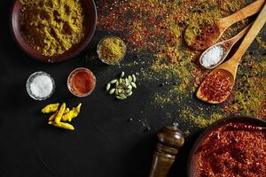 Set of indian spices on black background - green cardamom, turmeric powder, coriander seeds, cumin, and chili, top view photo