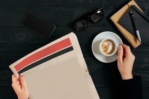 Young woman reading newspaper and holding coffee cup. photo