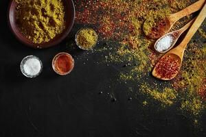 Set of indian spices on black background - green cardamom, turmeric powder, coriander seeds, cumin, and chili, top view photo