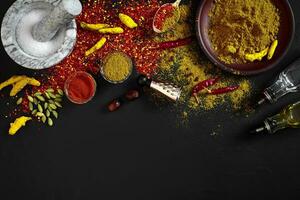 Cooking using fresh ground spices with mortar and small bowls of spice on a black table with powder spillage on its surface, overhead view with copyspace photo