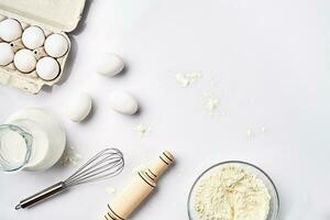 Wheat flour in the glass bowl, cream in a glass jar, chicken eggs - ingredients for the dough, top view photo