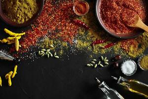 Set of indian spices on black background - green cardamom, turmeric powder, coriander seeds, cumin, and chili, top view photo