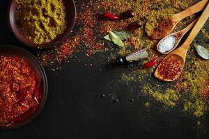 Set of indian spices on black background - green cardamom, turmeric powder, coriander seeds, cumin, and chili, top view photo