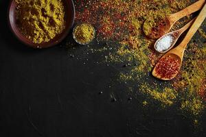 Set of indian spices on black background - green cardamom, turmeric powder, coriander seeds, cumin, and chili, top view photo