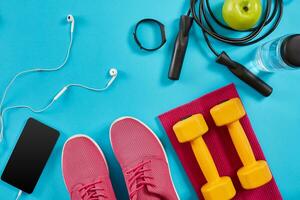 Flat lay shot of sneakers, jumping rope, dumbbells and smartphone on blue background. photo