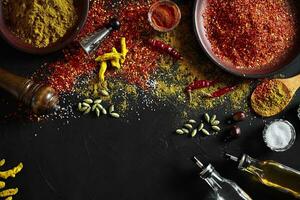 Cooking using fresh ground spices with big and small bowls of spice on a black table with powder spillage on its surface, overhead view with copyspace photo