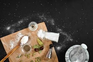 Marble mortar for spices, salt, cardamom and sprigs of bay leaf on a black background photo