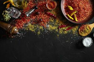 Cooking using fresh ground spices with big and small bowls of spice on a black table with powder spillage on its surface, overhead view with copyspace photo