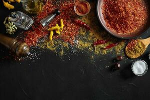 Cooking using fresh ground spices with big and small bowls of spice on a black table with powder spillage on its surface, overhead view with copyspace photo