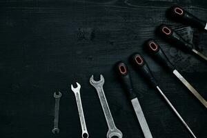 Series of many sharp steel blades and wrenches on black wooden background photo