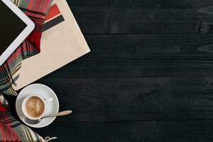 Above view of newspaper, scarf in a cage, tablet and cup of latte coffee on black wooden background. photo