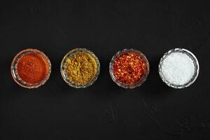 Cooking using fresh ground spices with four small bowls of spice on a black table overhead view with copyspace photo