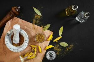 Turmeric Haldi powder in small bowl with raw whole in marble mortar over black background with copy space photo