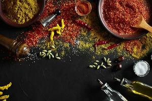Cooking using fresh ground spices with big and small bowls of spice on a black table with powder spillage on its surface, overhead view with copyspace photo