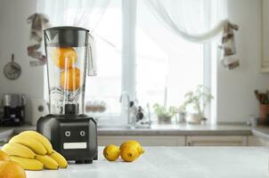 Metal food blender close-up with fresh exotic tropic fruits next to it on kitchen background with empty space photo