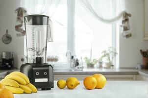 Metal food blender close-up with fresh exotic tropic fruits next to it on kitchen background with empty space photo