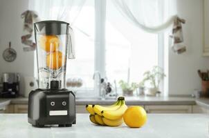 Metal food blender close-up with fresh exotic tropic fruits next to it on kitchen background with empty space. Sun flare photo