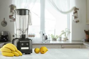 Metal food blender close-up with fresh exotic tropic fruits next to it on kitchen background with empty space photo