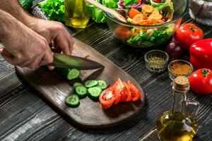 The man is cutting the cucumber in the kitchen in his house to prepare salad along with eating dinner. photo