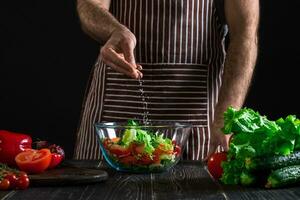 Man preparing healthy salad of fresh vegetables on a wooden table. photo