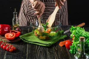 Man preparing salad with fresh vegetables on a wooden table. Cooking tasty and healthy food photo