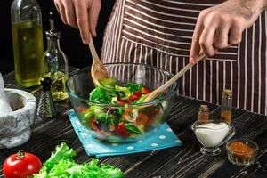 Man preparing salad with fresh vegetables on a wooden table. Cooking tasty and healthy food photo