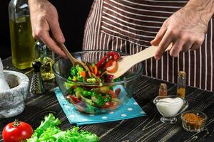 Man preparing salad with fresh vegetables on a wooden table. Cooking tasty and healthy food photo