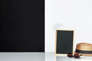 Blank blackboard and straw hat on table near white and black wall. photo