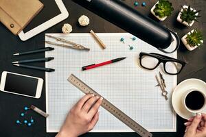 Office desk background hand with pen writing construction project ideas concept. With tablet, drawing equipment and a cup of coffee. View from above photo