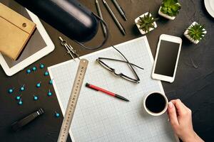 Office desk background hand with pen writing construction project ideas concept. With tablet, drawing equipment and a cup of coffee. View from above photo