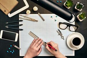 Office desk background hand with pen writing construction project ideas concept. With tablet, drawing equipment and a cup of coffee. View from above photo