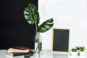 The stylish interior with mock up poster frame, leaves in glass bottle on table with black and white wall on background. photo