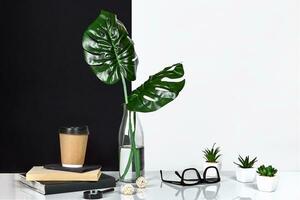 Hot coffee in brown paper cup and green leaves in glass bottle put on table with black and white wall on background photo