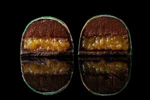 Cut luxury handmade candy with chocolate and yellow confiture filling on black background. photo