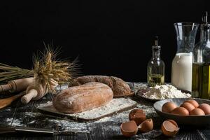 Beautiful still life with different kinds of bread, grain, flour on weight, ears of wheat, pitcher of milk and eggs photo