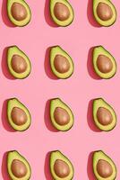 Colorful fruit pattern of fresh cutted avocado halves with pits on coral pink background, top view photo